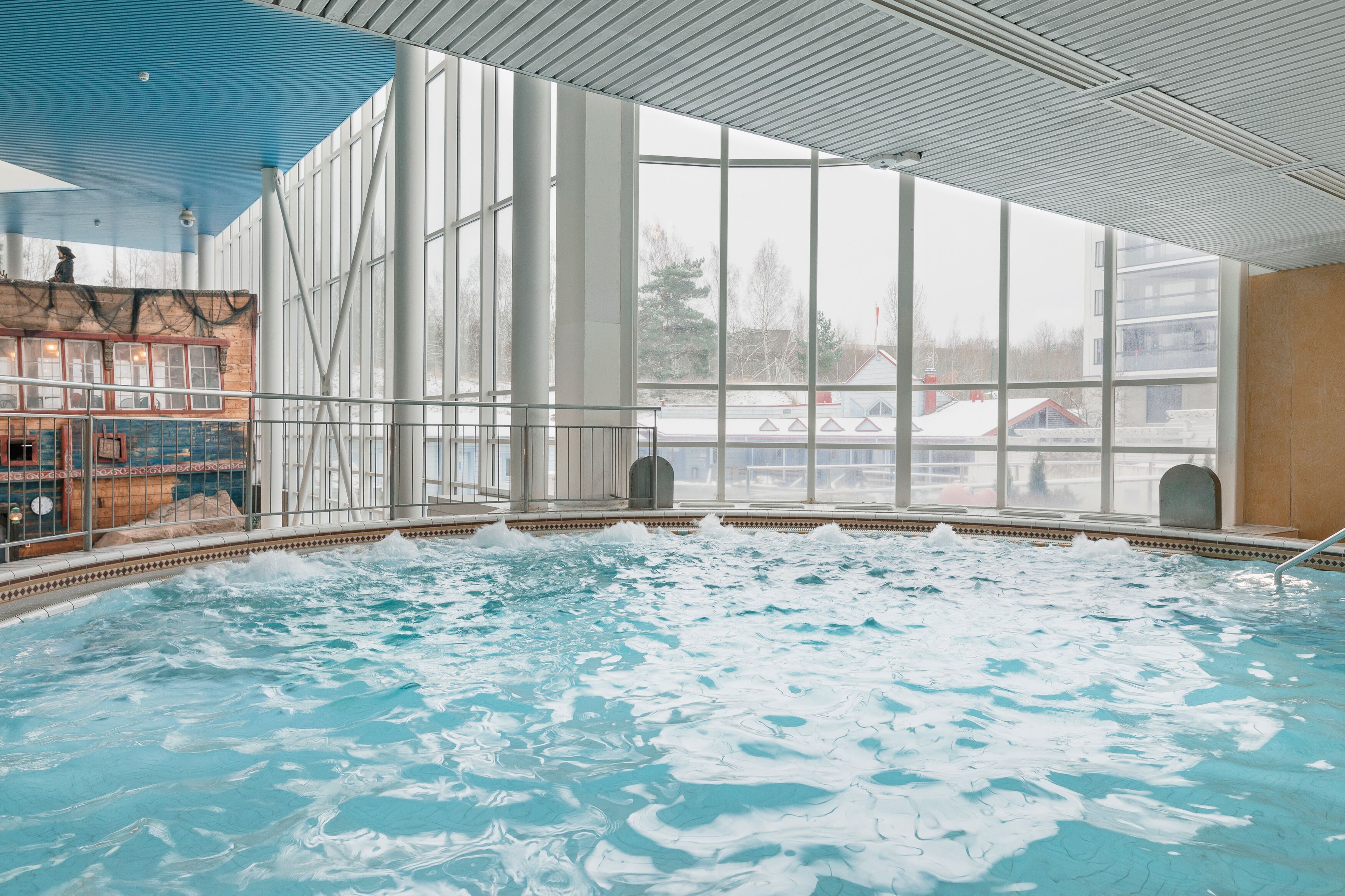 An indoor swimming pool with clear glass walls, a tiled floor, and a view of buildings outside.