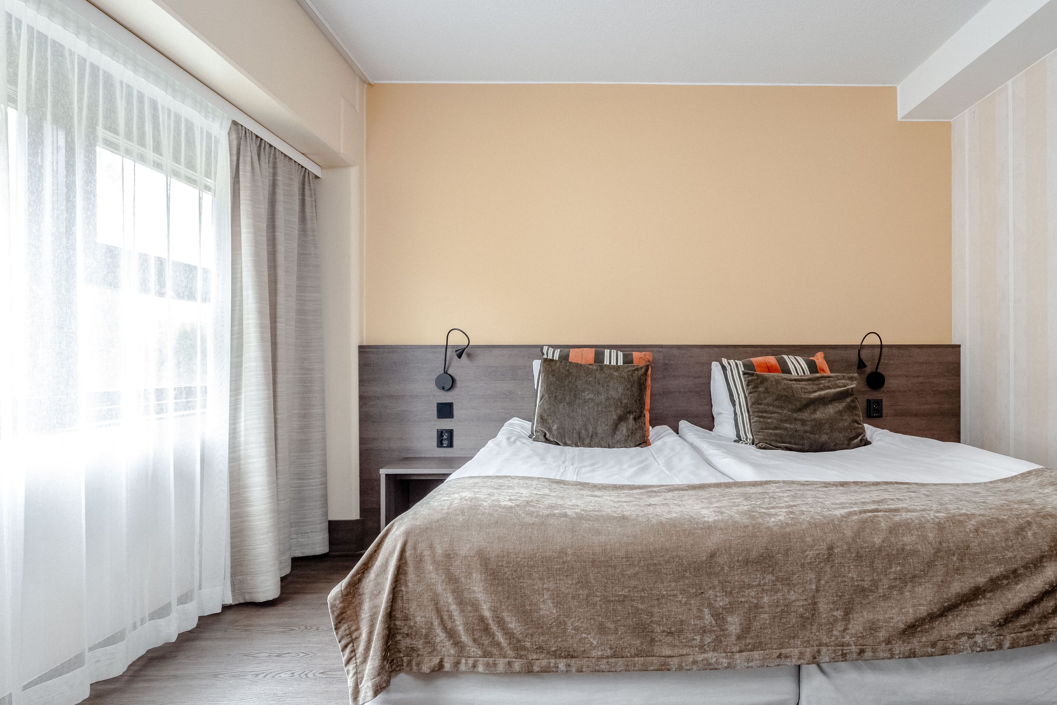 A hotel room with a large bed, a nightstand, and a wall-mounted lamp.