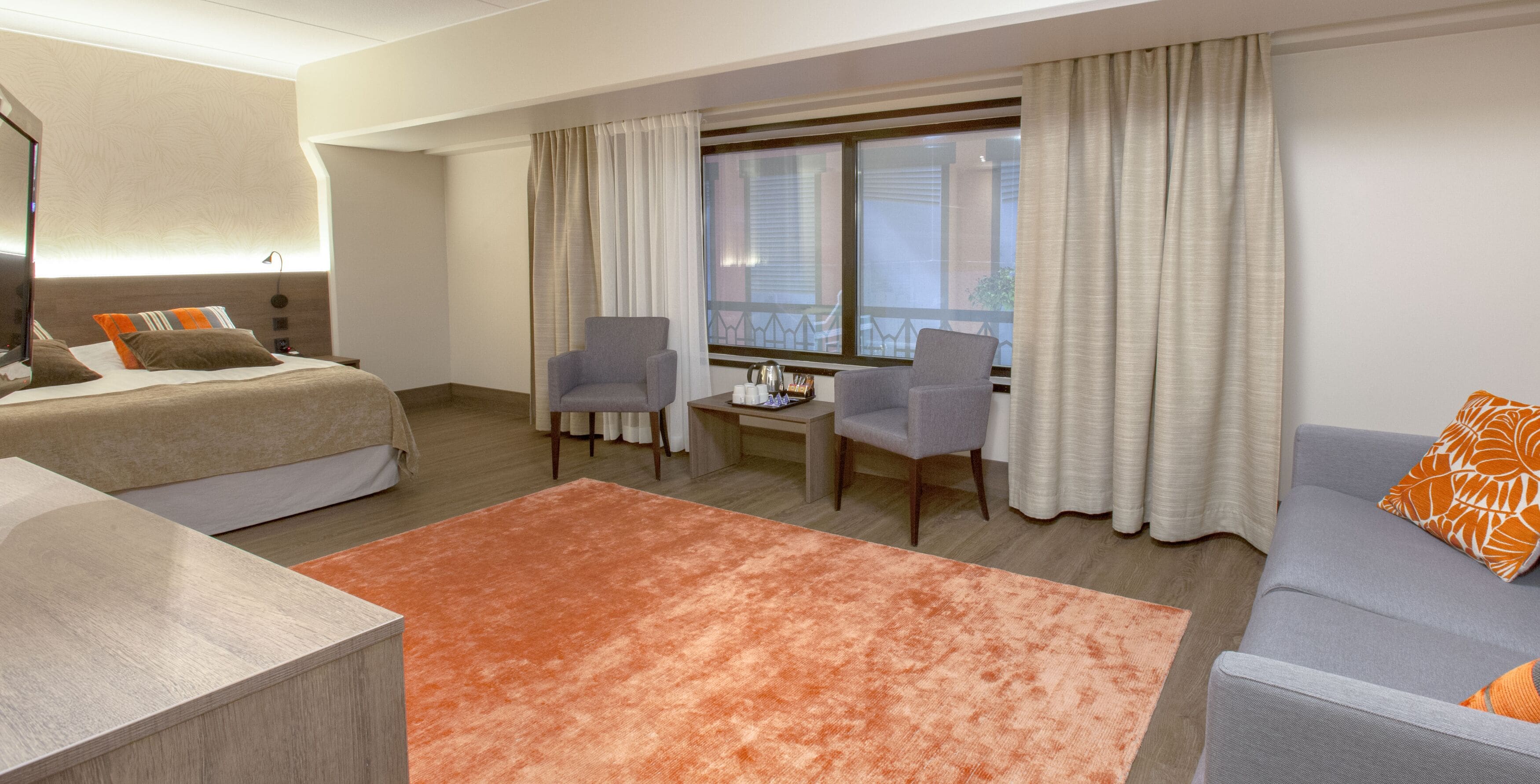 A hotel room with a bed, two armchairs, a sofa, a small table, and a window with curtains.