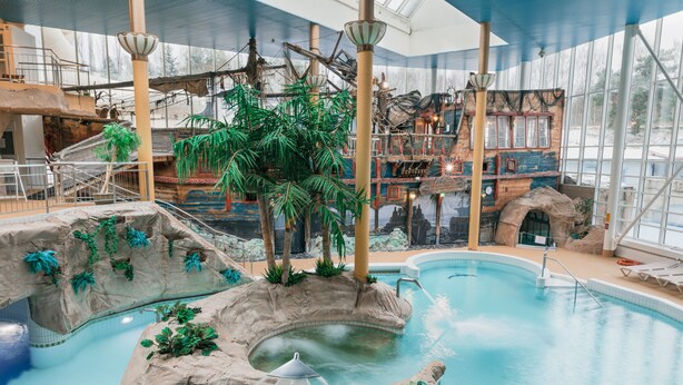 An indoor pool with a waterfall feature, surrounded by artificial rock formations and palm trees. - Holiday Club Turun Caribia (Turku)