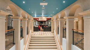 A grand staircase with a checkered floor leading to a reception area with a red counter and a sign indicating a restroom. - Holiday Club Turun Caribia (Turku)
