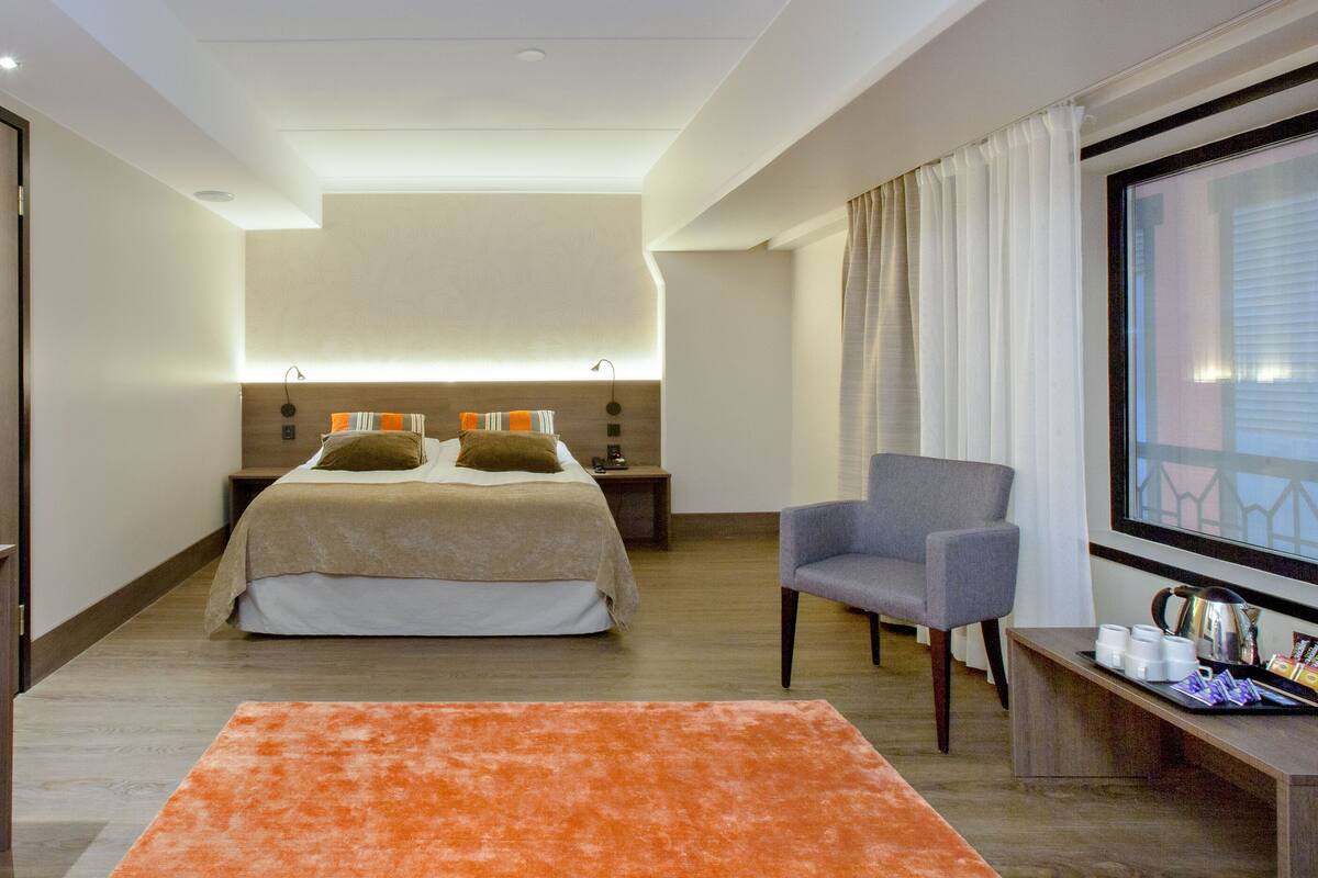 A modern hotel room with a bed, a seating area, a TV, and a window with curtains.