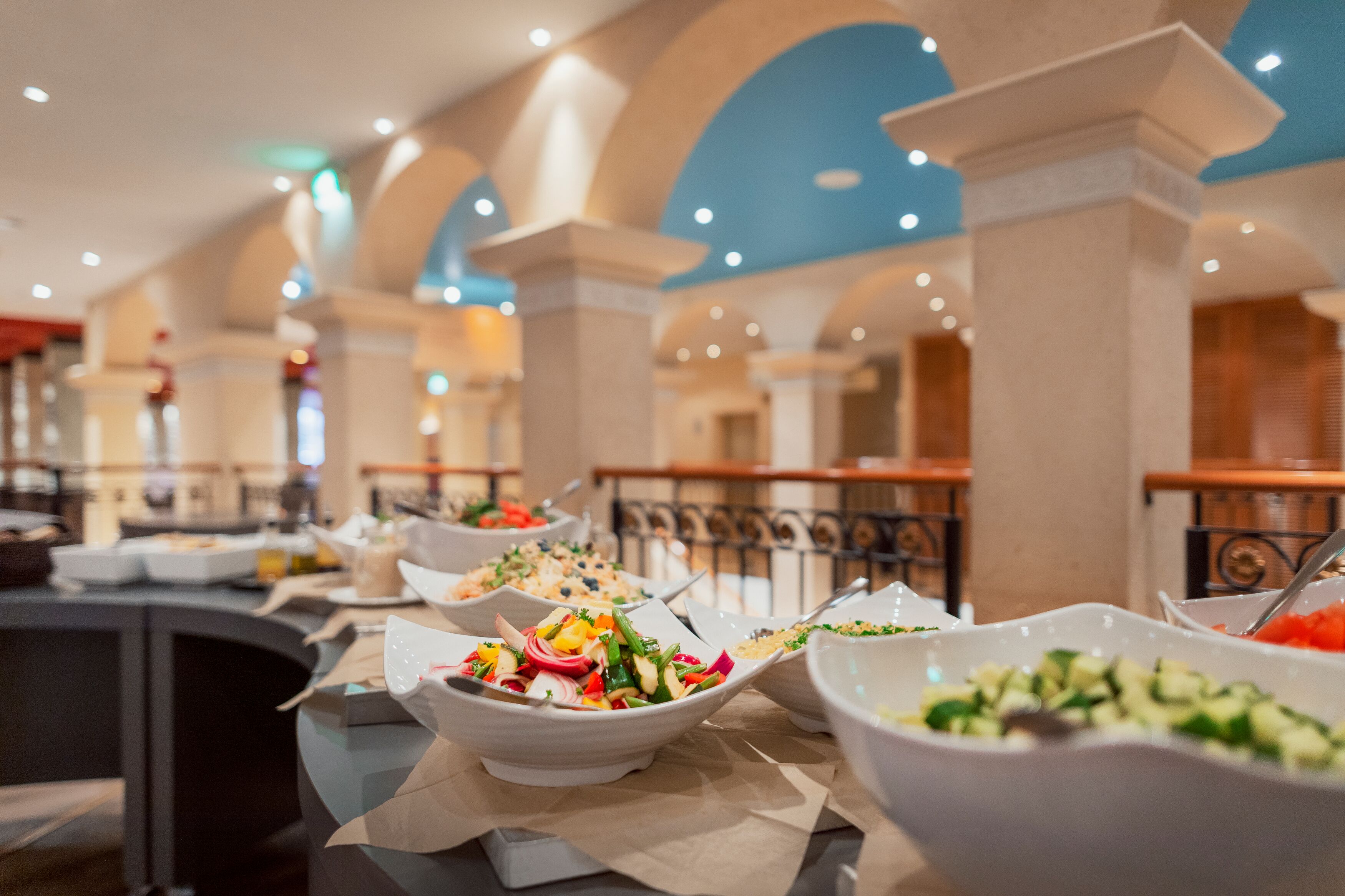 A buffet with various dishes, including salads and vegetables, in a room with arched ceilings and columns.
