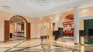 A spacious lobby with a geometric floor pattern, a reception area with a counter and chairs, and a seating area with a fireplace.