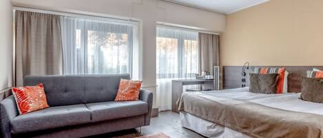 Una habitación de hotel moderna con un sofá gris, una cama grande y un escritorio.