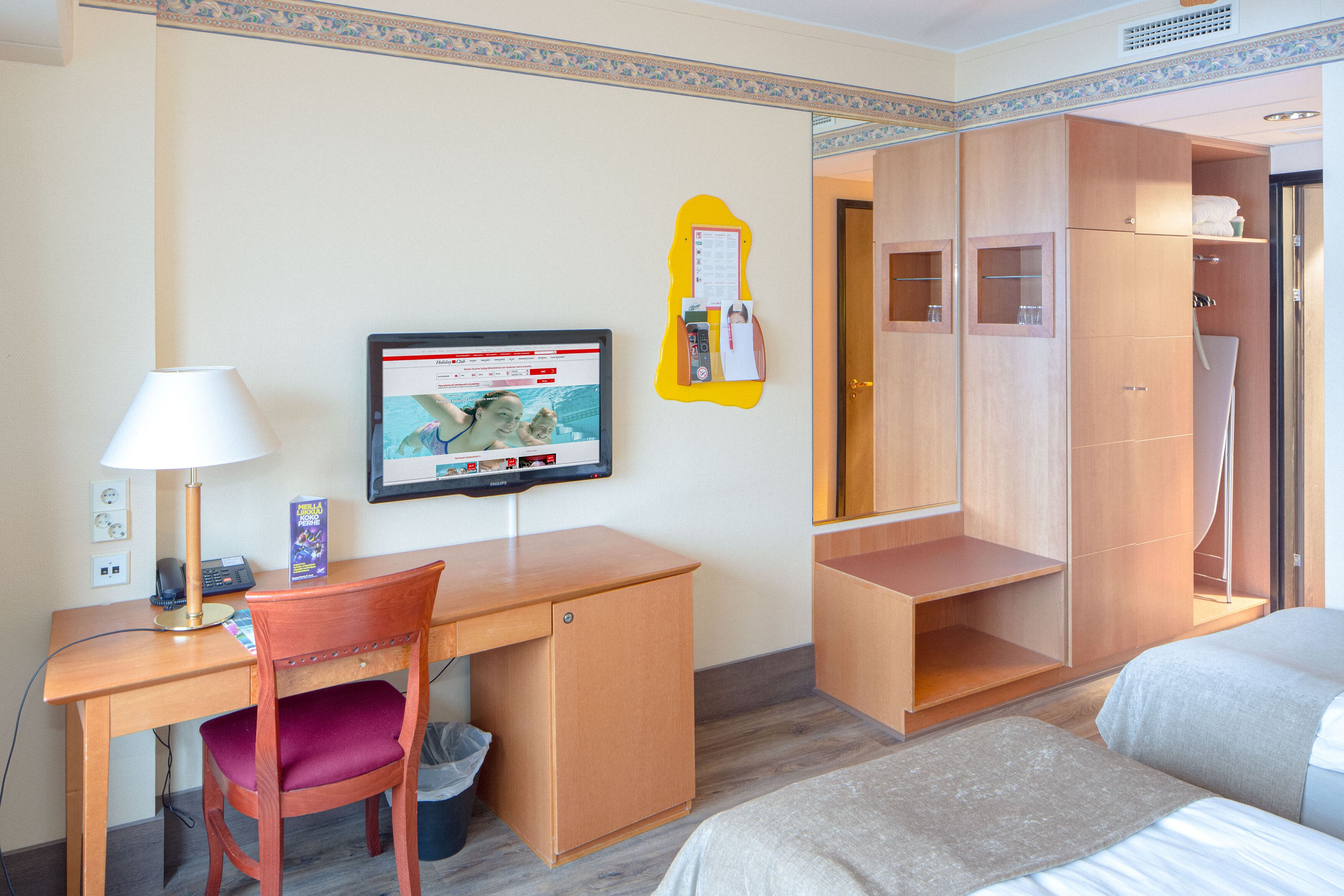 Una habitación de hotel con un escritorio de madera, televisor, armario y cama.