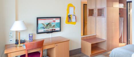 Una habitación de hotel con un escritorio de madera, televisor, armario y cama.