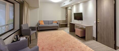 A modern living room with a sofa, armchairs, a coffee table, a flat-screen TV, and a large rug.