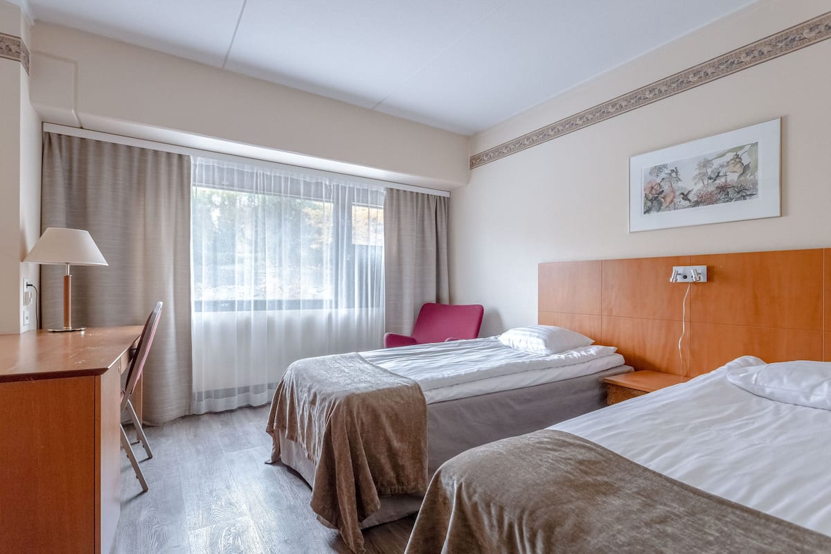 A hotel room with two beds, a desk, a chair, and a window with curtains.