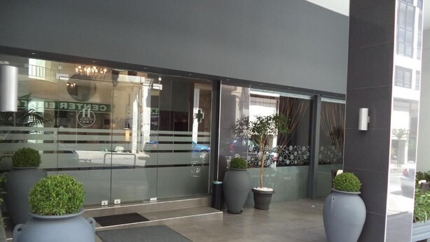Una entrada de edificio moderna con grandes puertas de cristal, plantas en macetas y un cartel que dice 'CENTRE'.