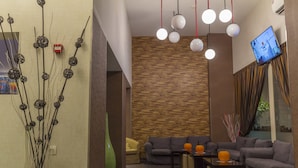 Una moderna área de recepción con un espacio de descanso, un televisor grande montado en la pared y una planta decorativa.