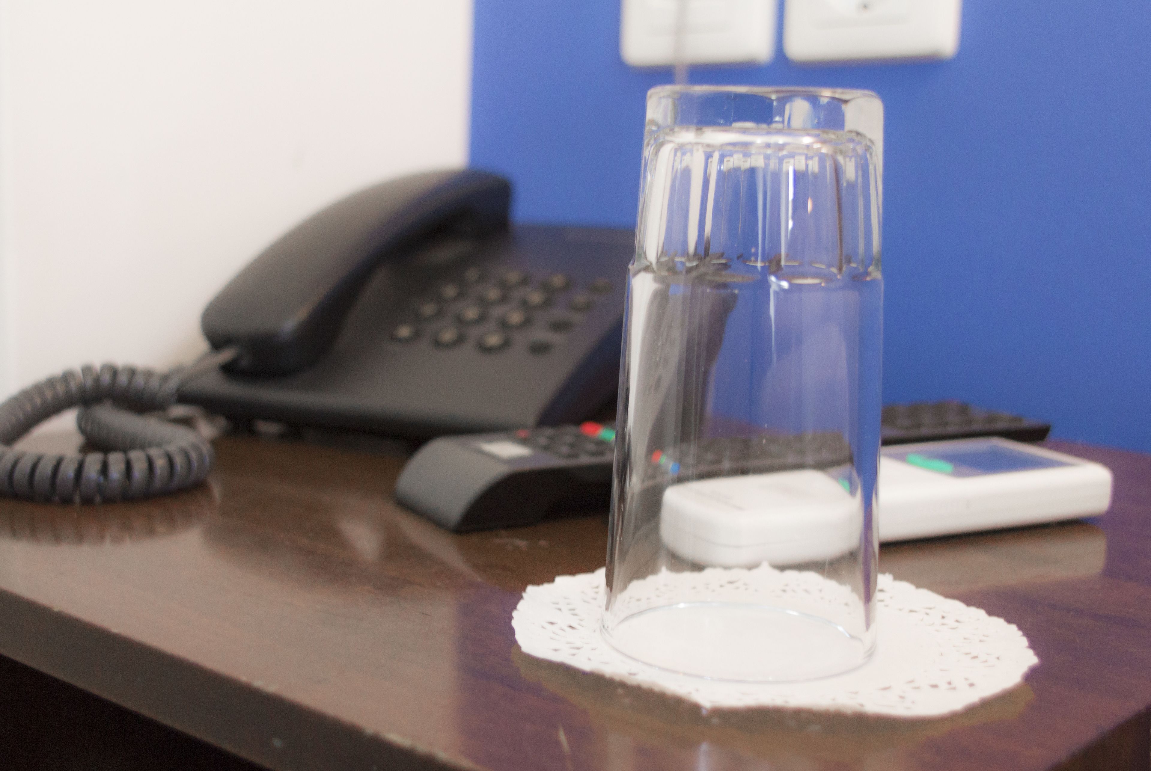 A glass of water on a doily atop a wooden desk, with a telephone and a calculator in the background.