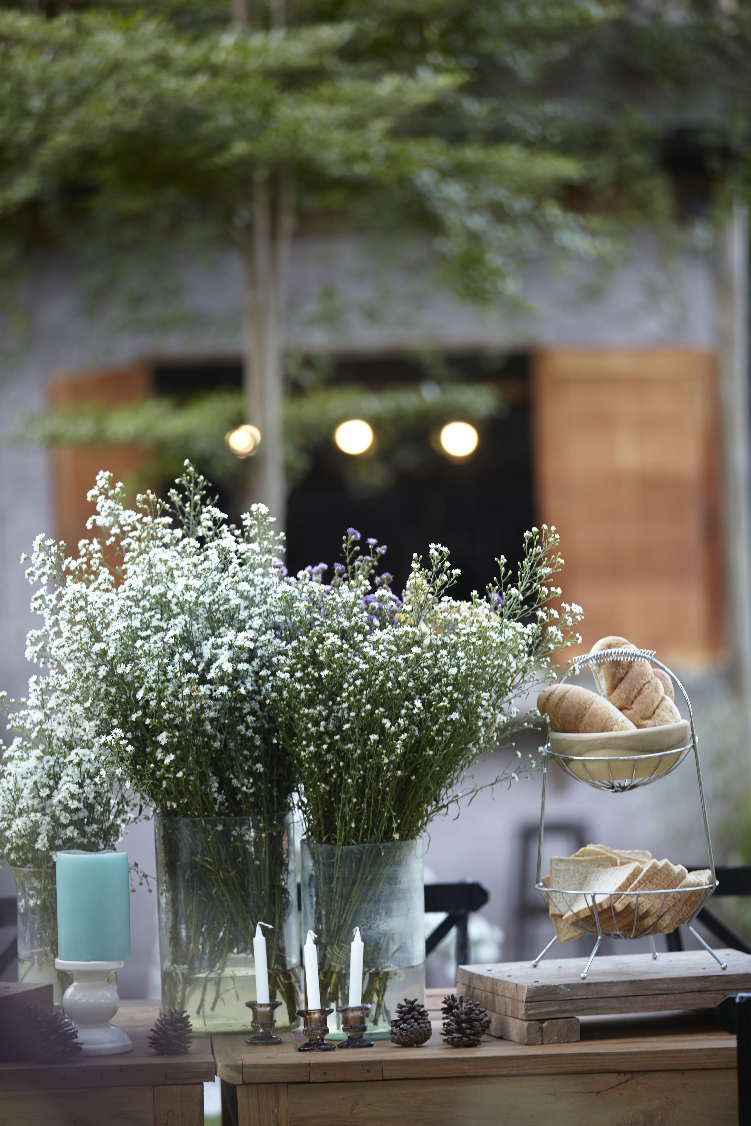 A table with a candle, a vase with flowers, and bread on a wooden board.