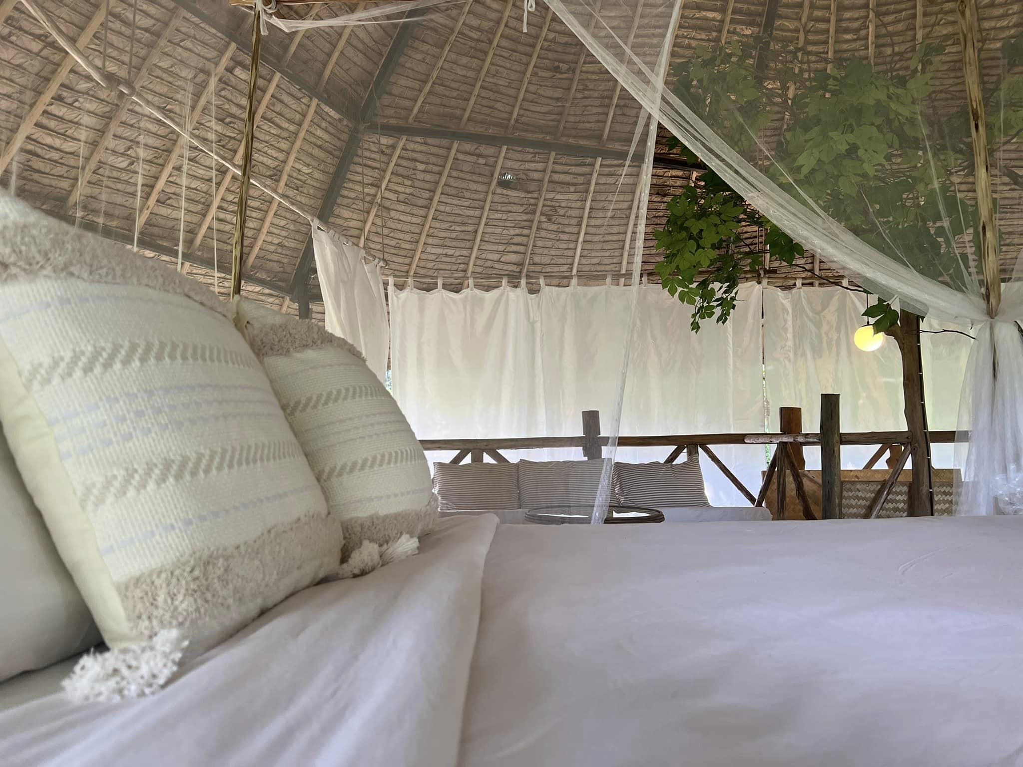 Una cama con ropa blanca y dosel, techo de madera y vistas al verdor exterior.