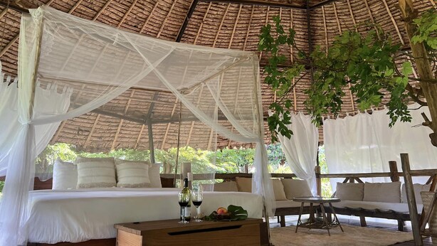 A thatched-roof tent with a canopy bed, a wooden table with drinks, and a seating area. - House of Love at Pai (Pai)