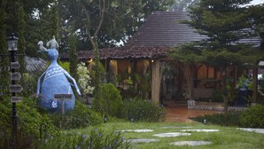 A garden with a large blue sculpture, a wooden house, and stone pathways. - House of Love at Pai (Pai)