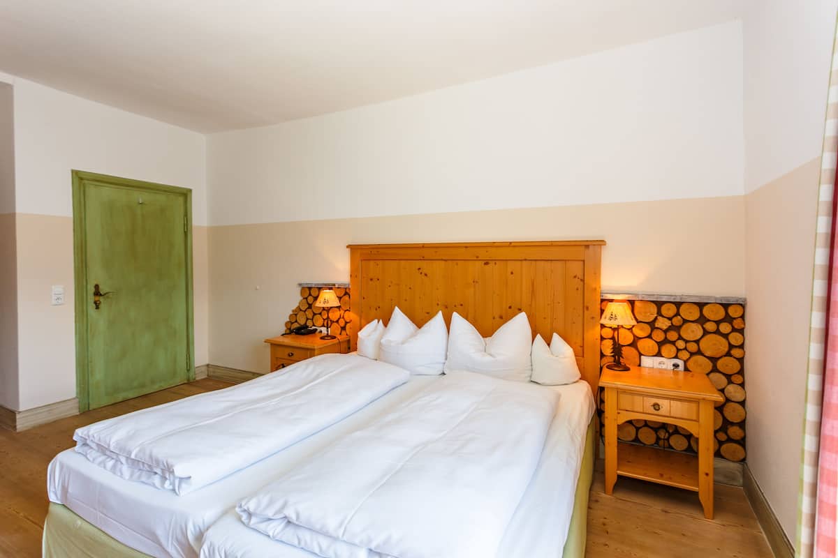 A double bed with white linens, a wooden headboard, two bedside tables with lamps, and a green door.