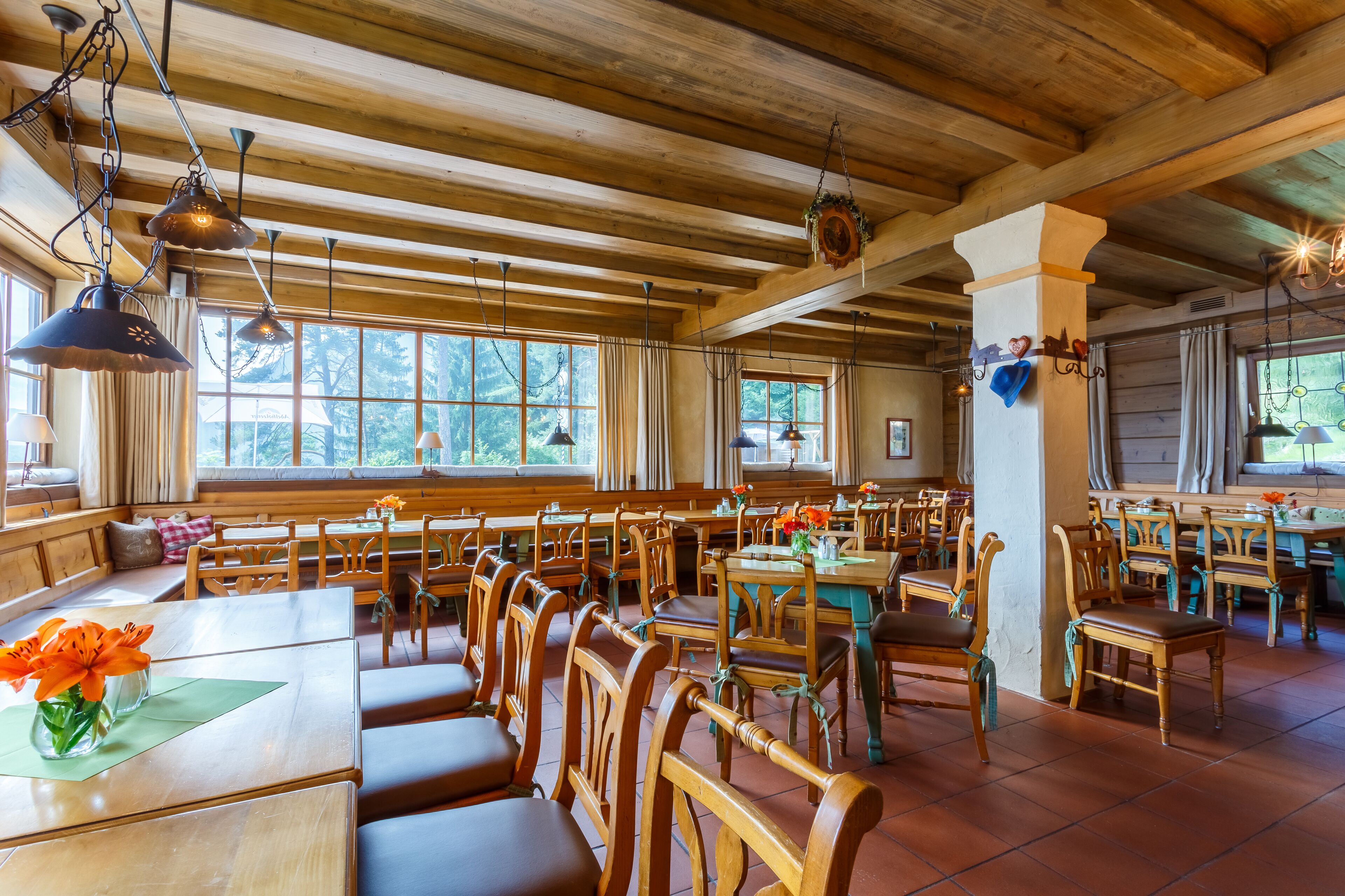 A spacious dining area with wooden tables and chairs, large windows with curtains, and hanging pendant lights.