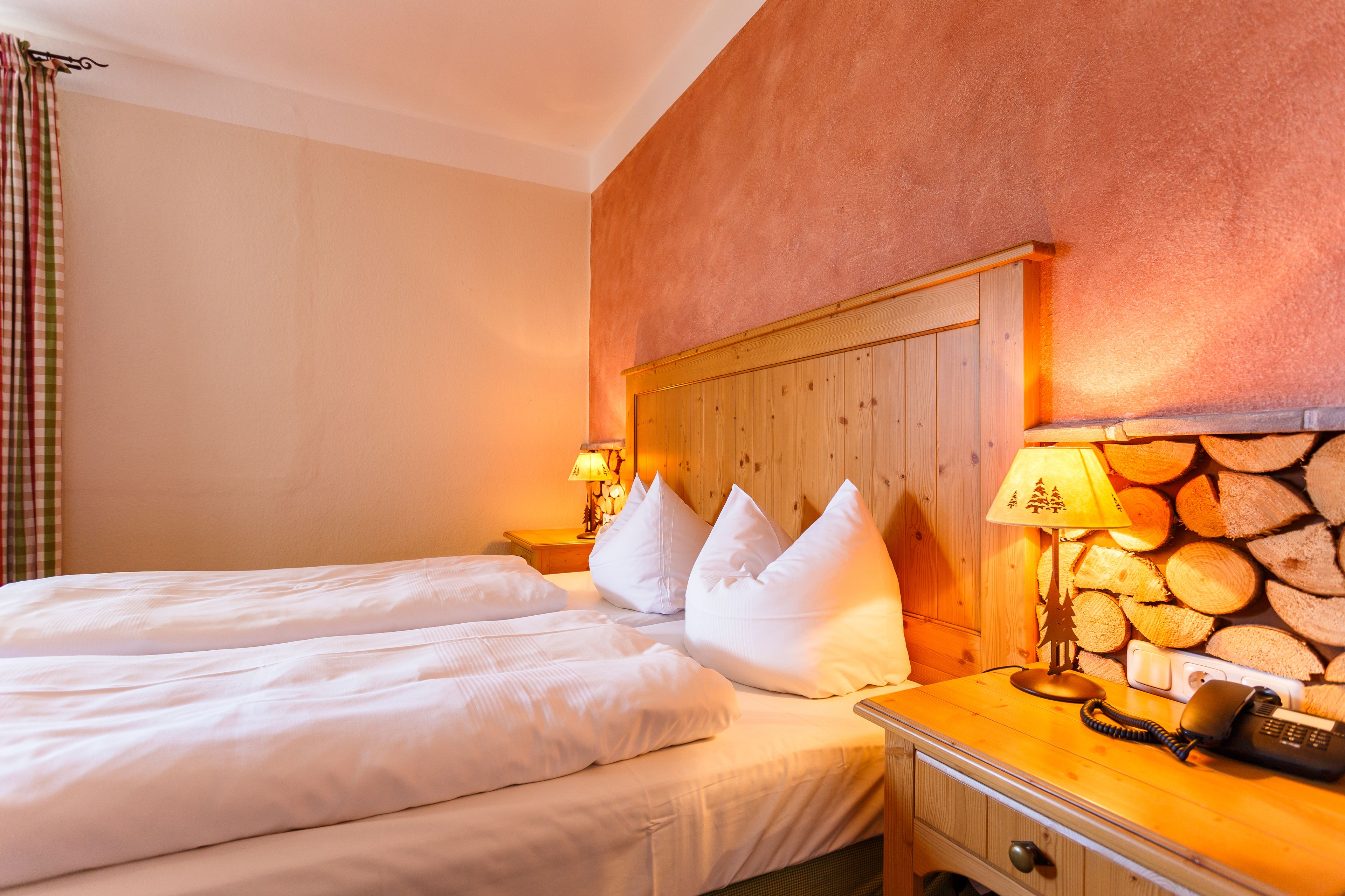Quarto de hotel com cabeceira de madeira, duas camas com roupa de cama branca, mesa de cabeceira com abajur e telefone.