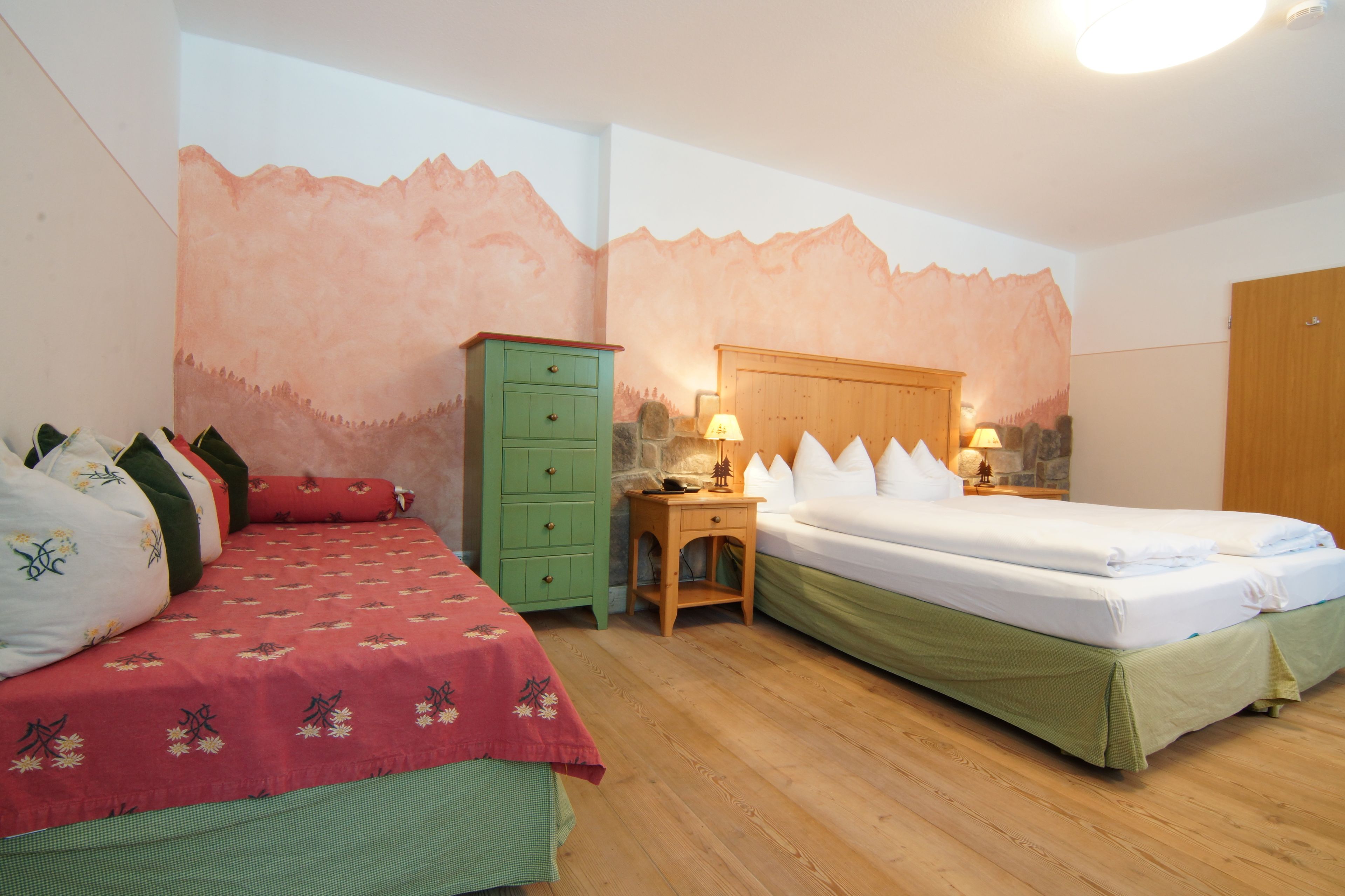 A bedroom with two beds, a green dresser, and a wooden nightstand with lamps.