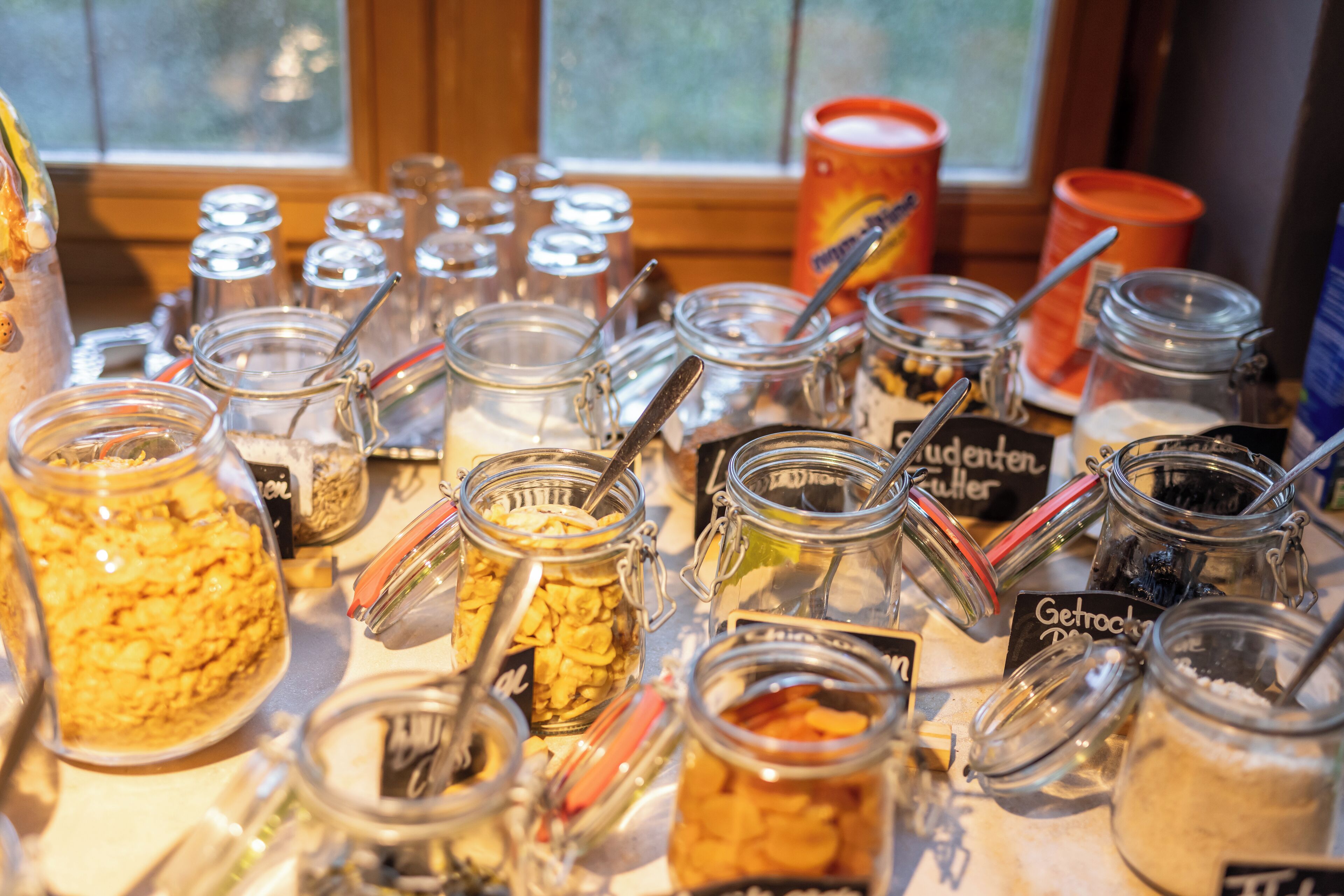 A variety of food items in glass jars with metal lids and spoons, some labeled in a foreign language.