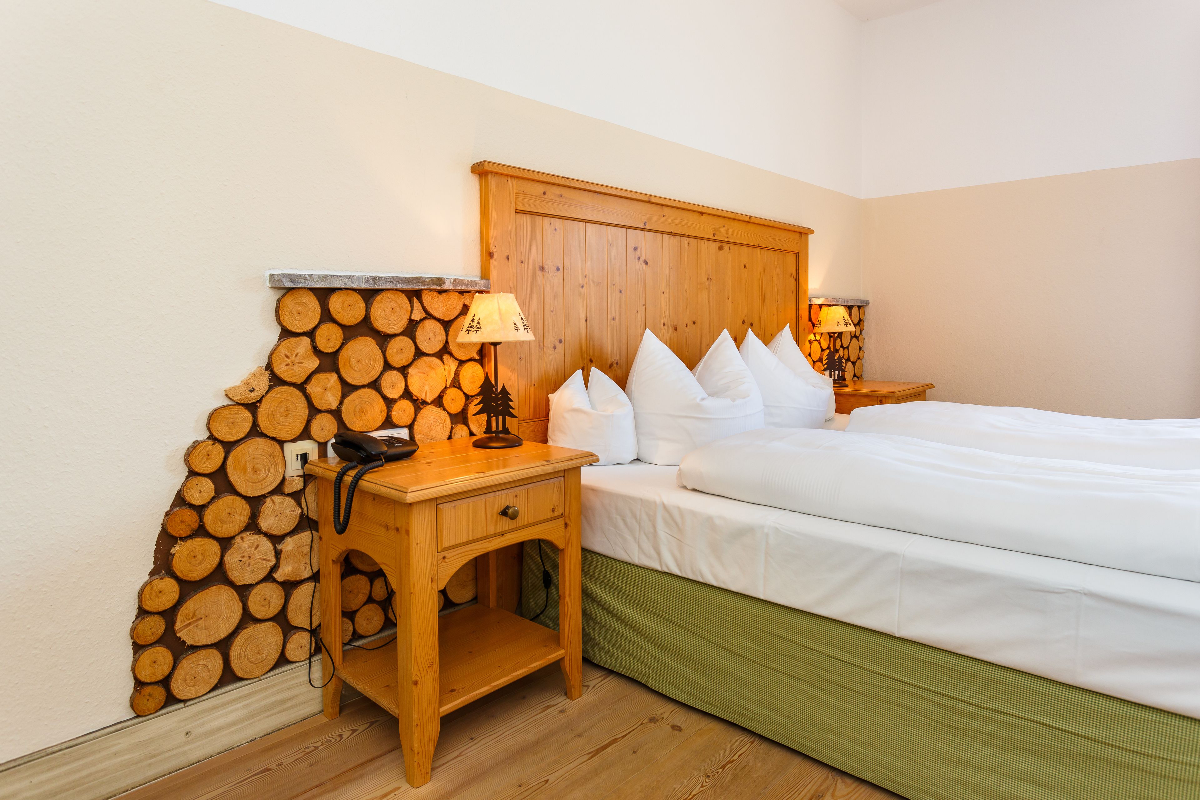 A bedroom with a wooden headboard, a bedside table with a lamp, and a wall decorated with stacked logs.