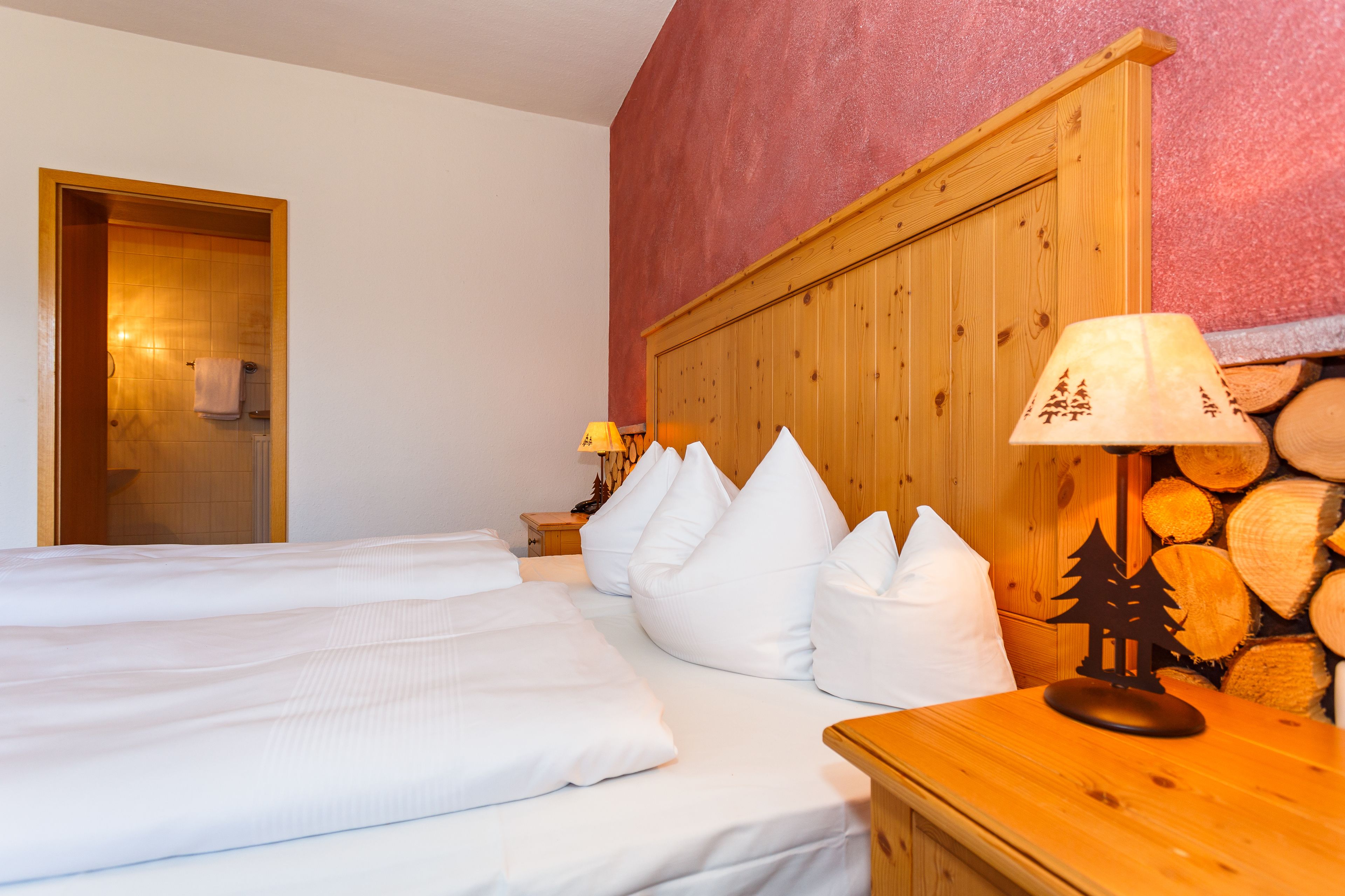 Hotellihuone, jossa on kaksi sänkyä, puinen pääty, valkoiset vuodevaatteet, yöpöytä lampulla ja puinen seinä.