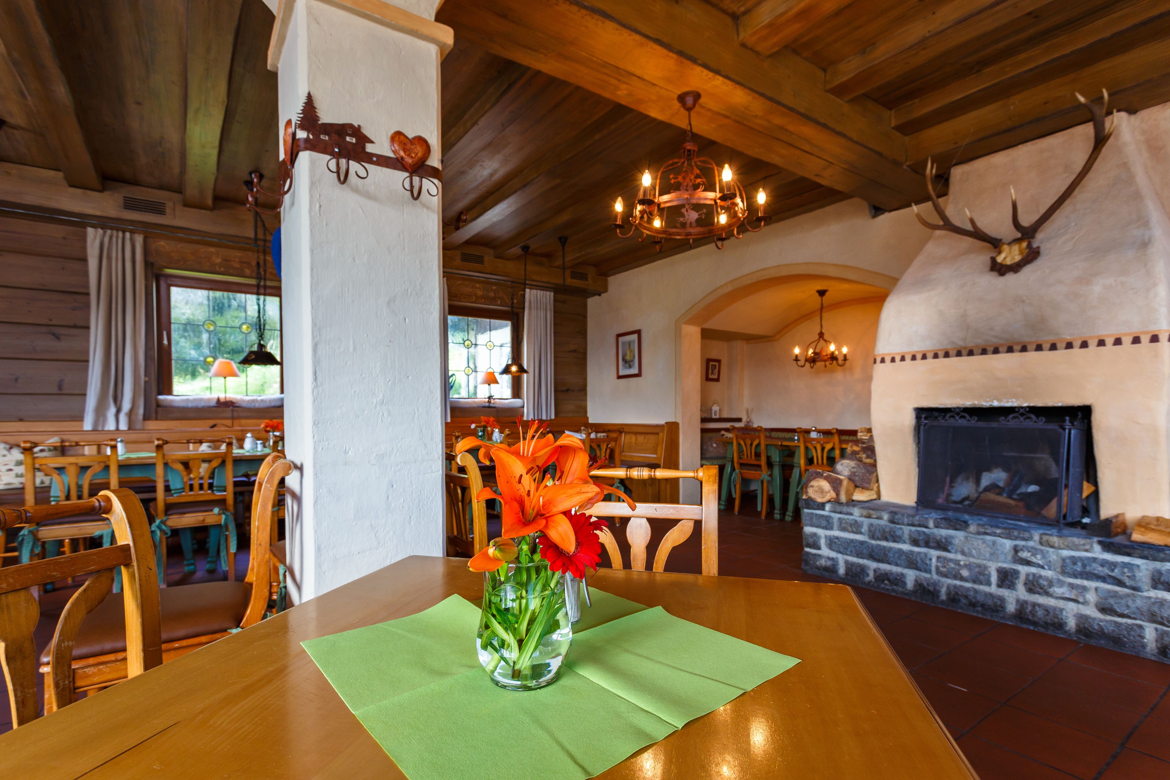 Una mesa de comedor de madera con un florero, sillas de madera, una chimenea y una araña en un interior rústico.