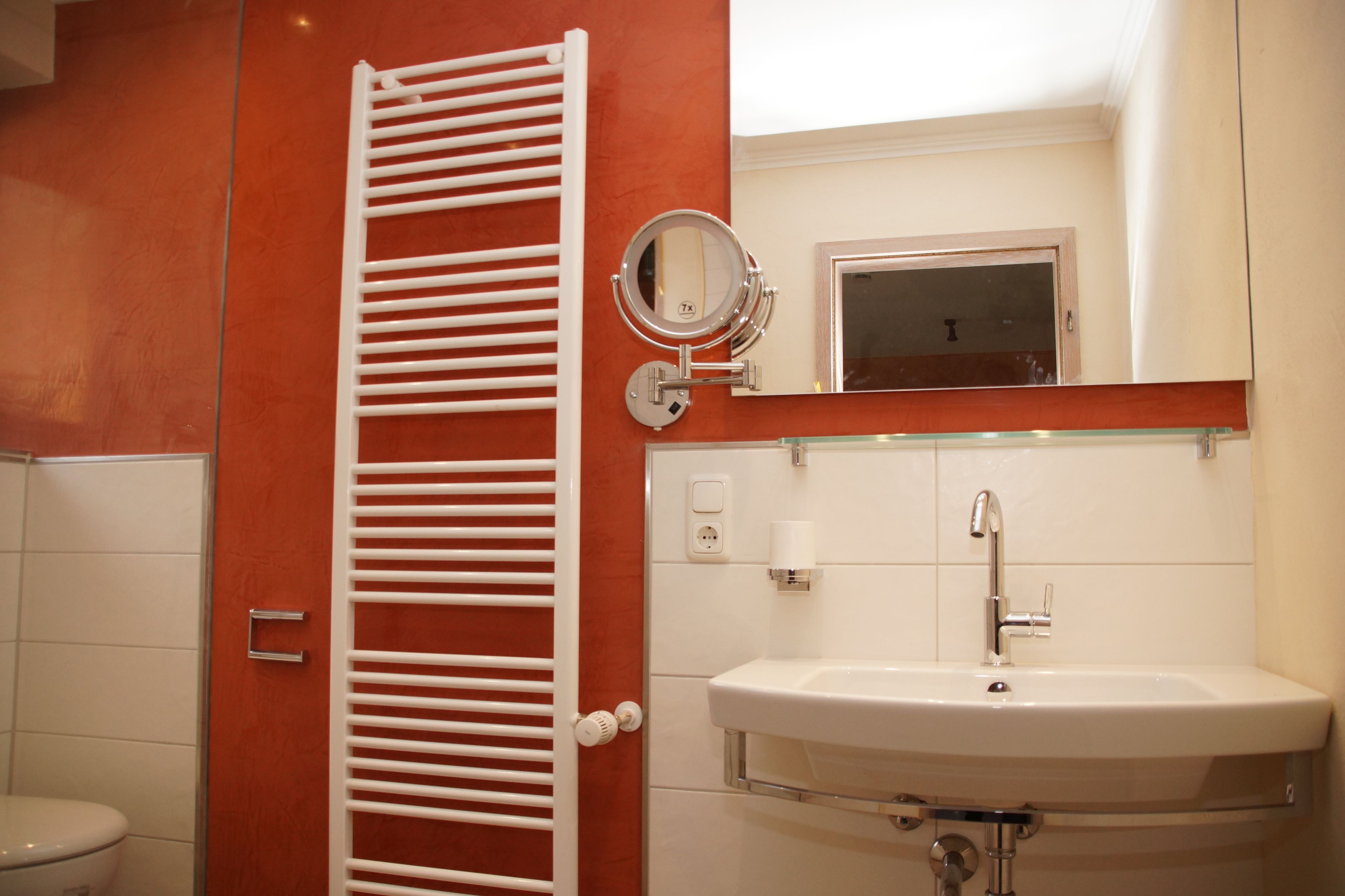 A bathroom with a white toilet, a white towel rack, a white sink with a mirror above it, and a red wall.