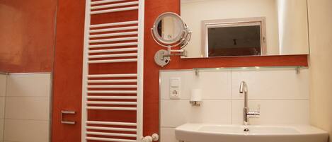 A bathroom with a white toilet, a white towel rack, a white sink with a mirror above it, and a red wall.