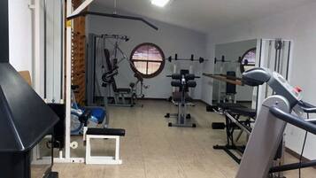 Ein Fitnessstudio mit verschiedenen Trainingsgeräten, darunter Laufband, Kraftgeräte und eine Trainingsbank.