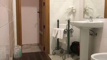 Un baño con puerta de madera, paredes cubiertas de azulejos blancos, un lavamanos con espejo y una pequeña mesa con velas.
