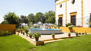 A courtyard with a fountain, potted plants, and a building with yellow and white walls.