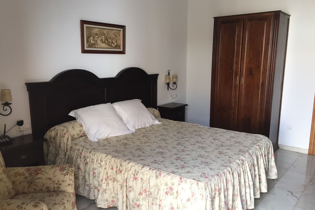A bedroom with a bed, a nightstand, a chair, a wardrobe, and a wall-mounted picture.