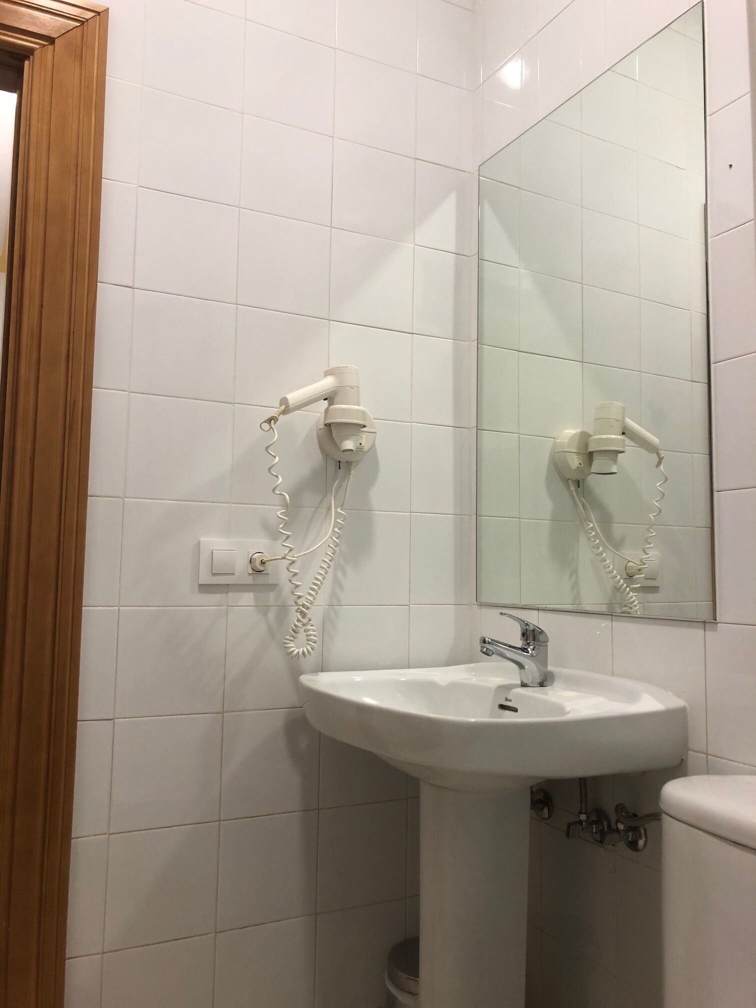 Un baño con azulejos blancos, un lavabo, un espejo y un secador de pelo montado en la pared.