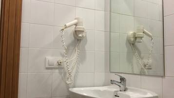 Un baño con azulejos blancos, un lavabo, un espejo y un secador de pelo montado en la pared.