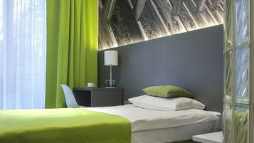 A hotel room with a bed, a desk, a lamp, and a large window with curtains.