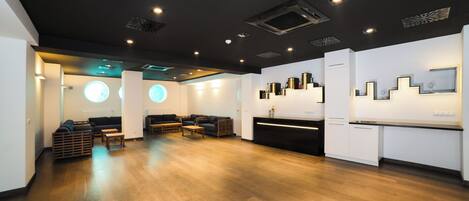 A modern interior with a wooden floor, a reception desk, and seating areas.