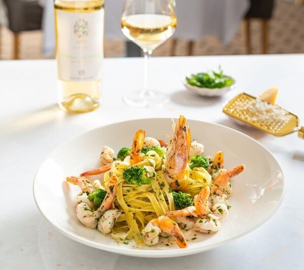 A plate of pasta with shrimp and broccoli, a glass of white wine, and a salt grinder on a table.