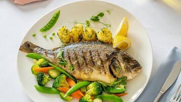 Un plato con pescado a la parrilla, papas y verduras variadas.