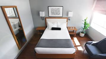 A neatly arranged hotel room with a large bed, bedside tables, a mirror, a chair, and a potted plant.