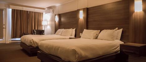 Habitación de hotel con dos camas, un escritorio, una silla y un ventanal con cortinas.