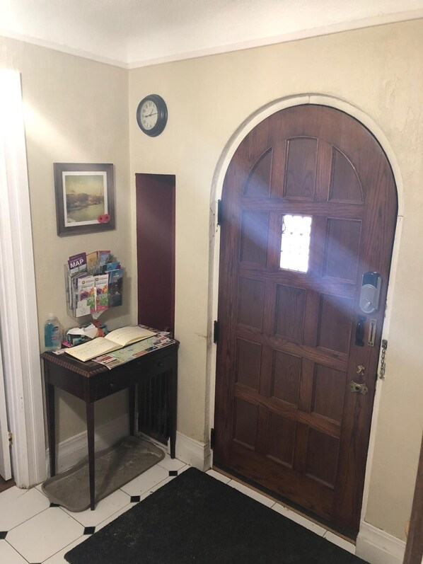 A wooden door with a glass panel, a clock on the wall, a framed picture, and a table with various items including a map and a bottle.
