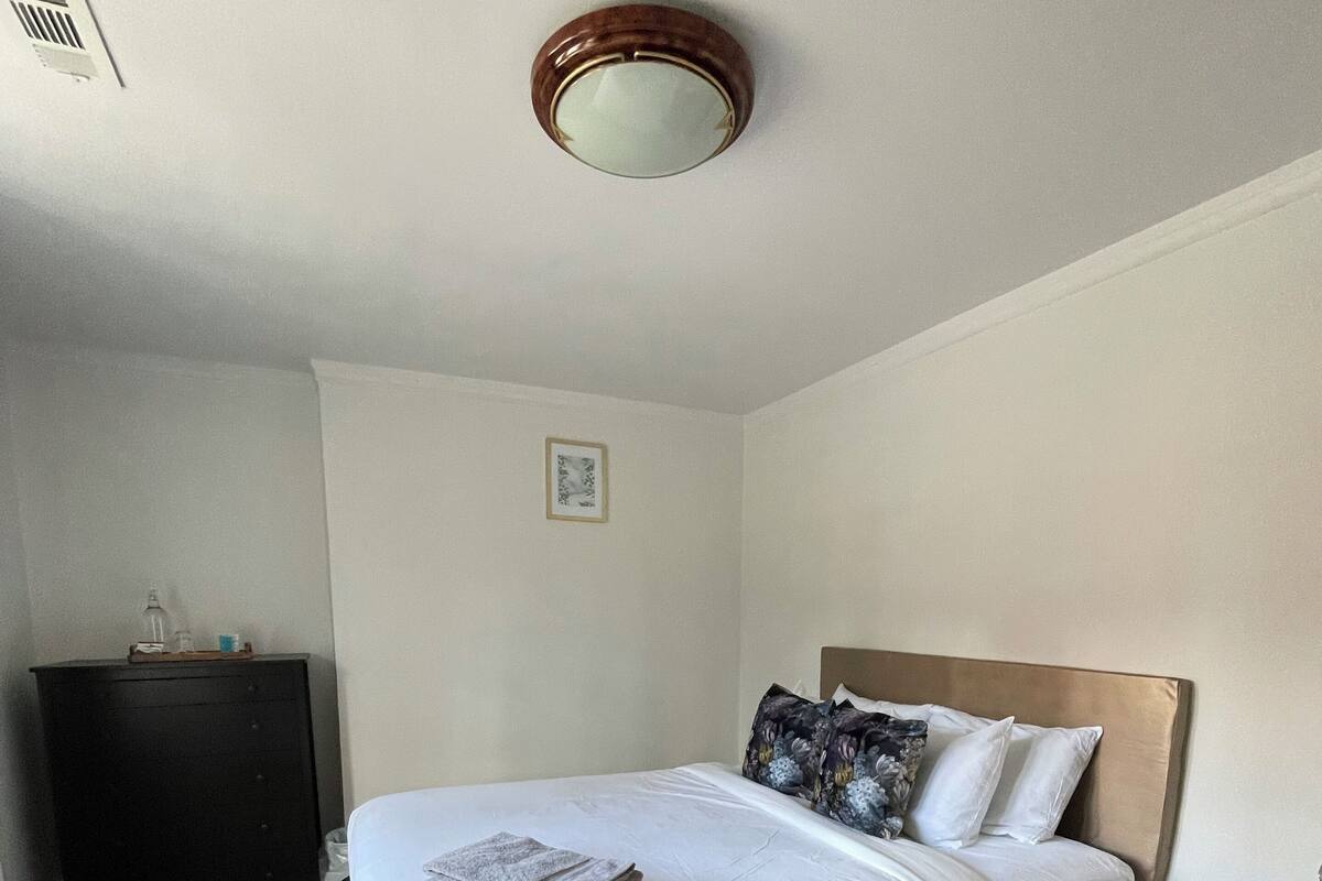 A neatly made bed with a wooden headboard, a bedside table, and a small stool.
