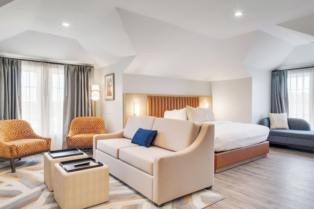 A hotel room with a sofa, two armchairs, a bed, and a coffee table.