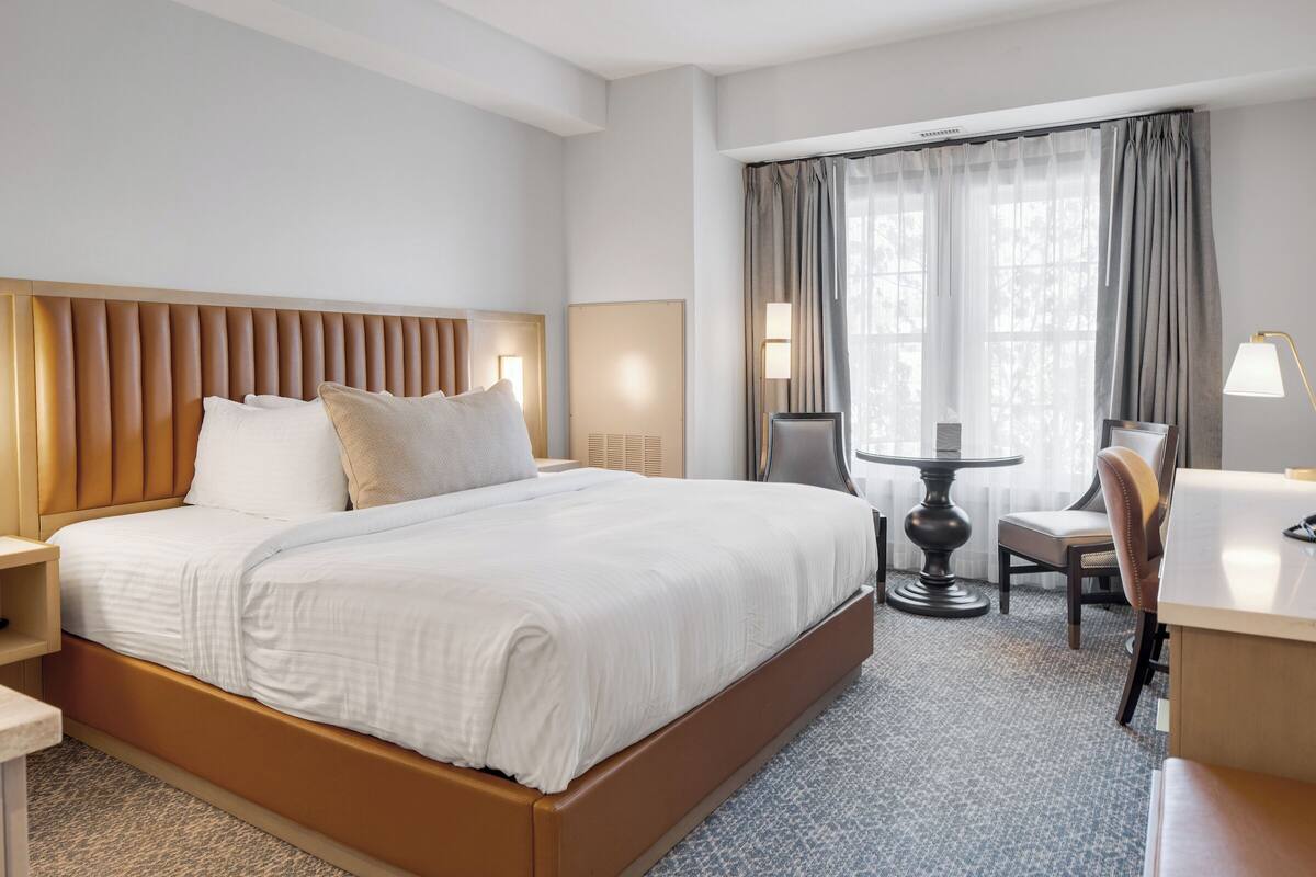 A hotel room with a large bed, a desk, a chair, and a small table.