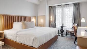 A hotel room with a large bed, a desk, a chair, and a small table.