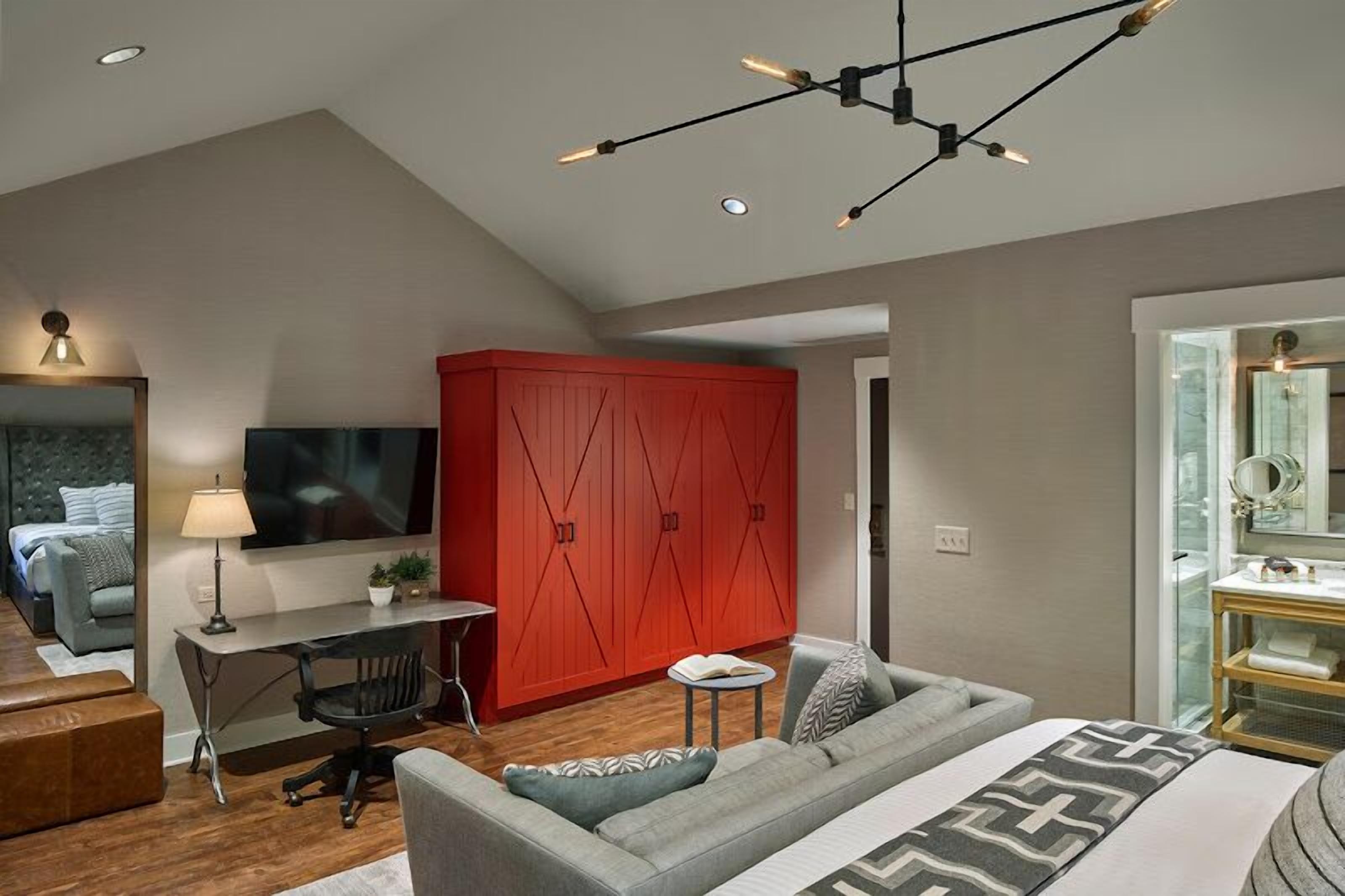 A modern bedroom with a bed, a desk, a red wardrobe, and a TV.