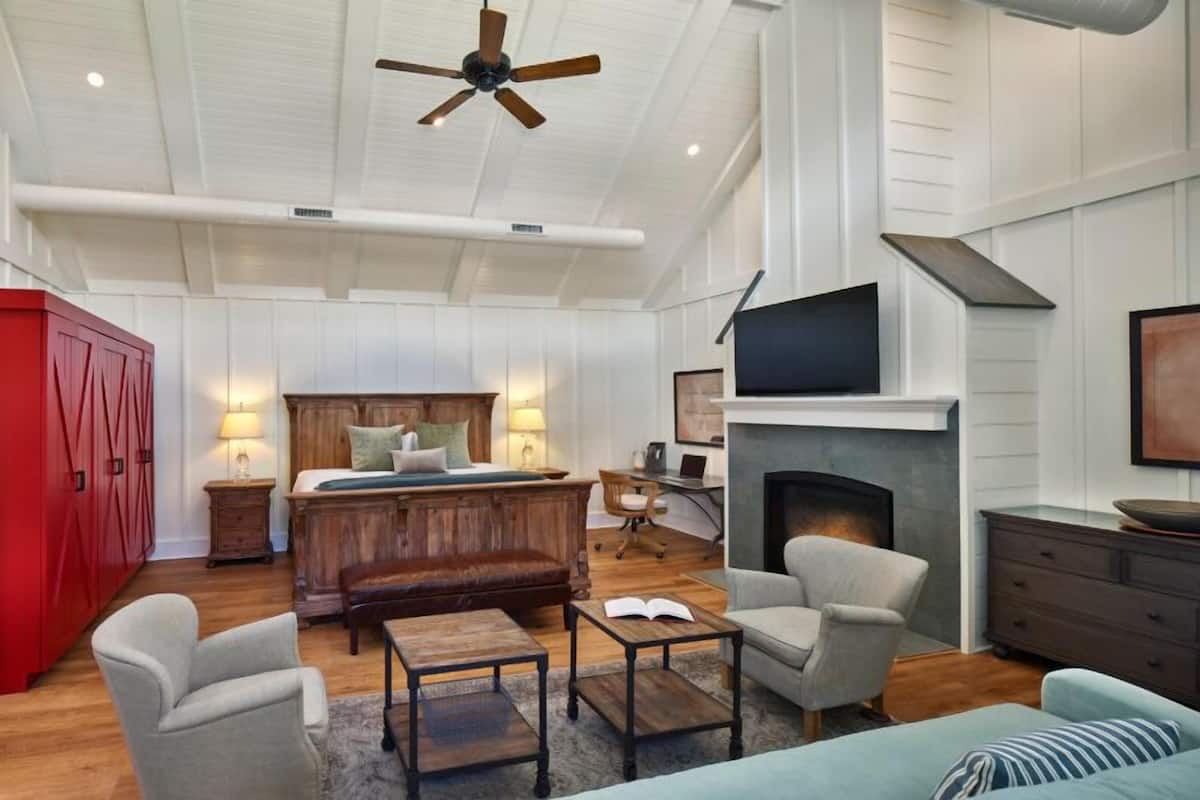 A spacious room with a large bed, a fireplace, a desk, and a TV mounted on the wall.