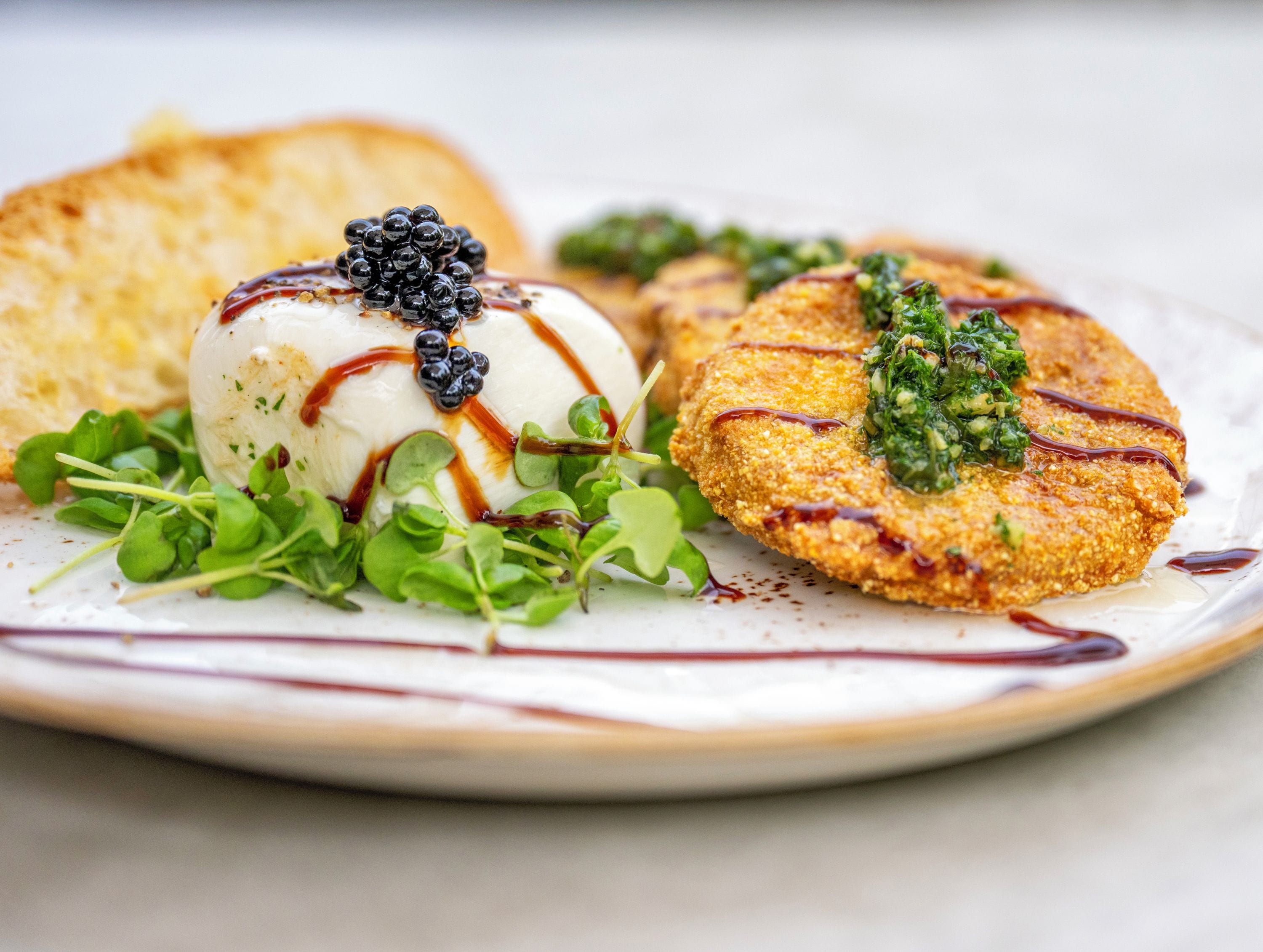 A plate with a poached egg, blackberries, and a breaded item with greens and sauce.